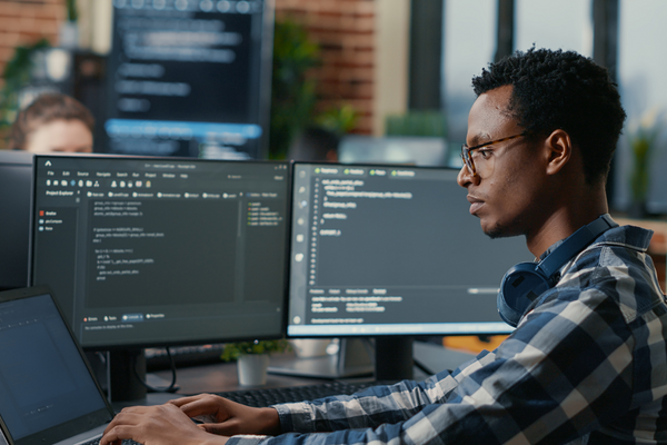 A man sitting at a desk with multiple computer screens coding