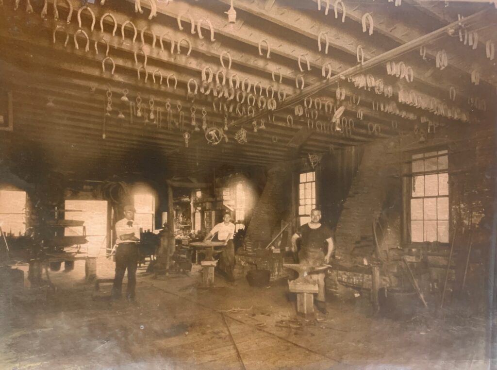 An old black and white photo of workers smithing horseshoes. 