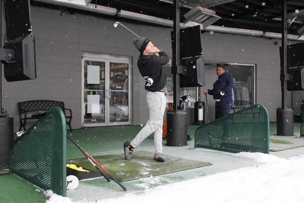 A UM-Flint student who plays in the Club Golf team swings at a golf ball while another student watches.