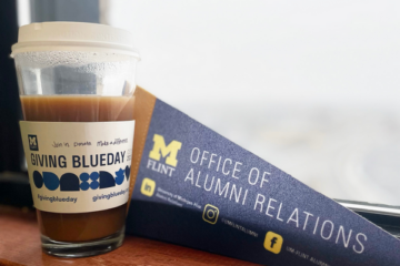 A coffee cup with sleeve that says Giving Blueday on a windowsill next to an Office of Alumni Relations pennant.