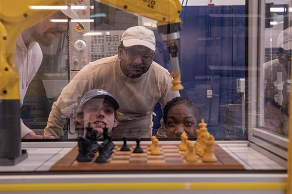 Students watching a robotic arm play chess