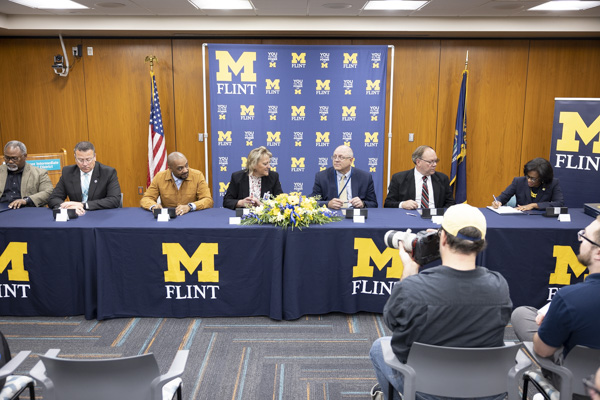 A group of people at a table with a UM-Flint tablecloth signing an agreement