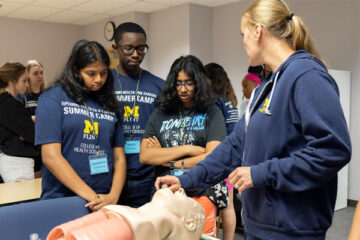 Three high school students and a UM-Flint nurse anesthesia student gather around a mannequin and learn about opening airways