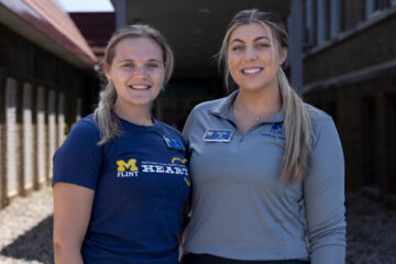 Picture of physical therapy students Olivia Roe and Brooke Mazzolini posing in front of Sylvester Broome Empowerment Village in Flint