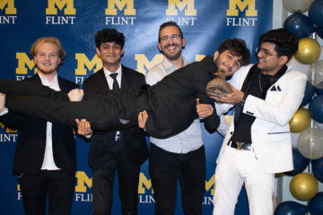 A group of students posing in front of a UM-Flint banner