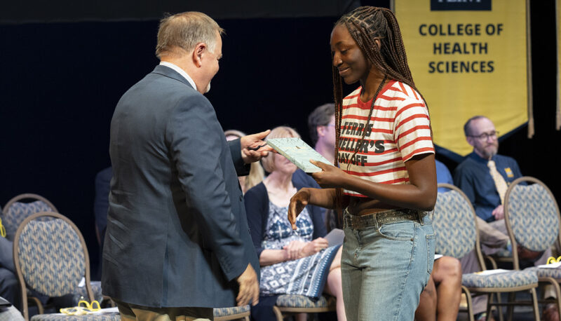 A student receiving a book on stage from Tom Wrobel