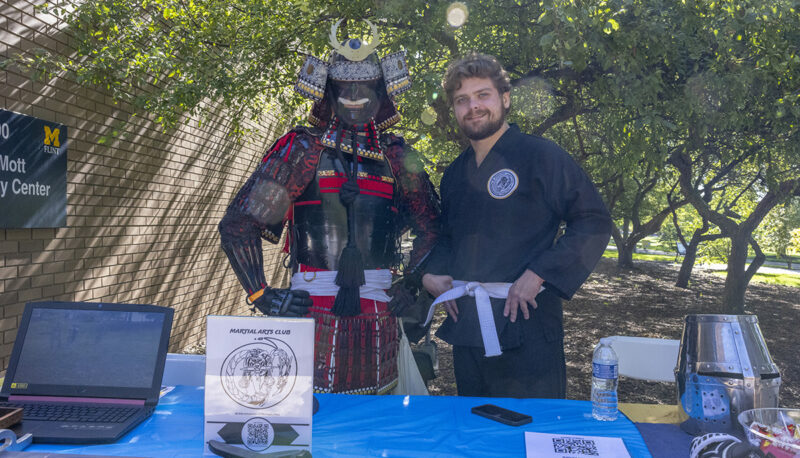 A person in samurai armor standing next to a person in a martial arts uniform behind a table.