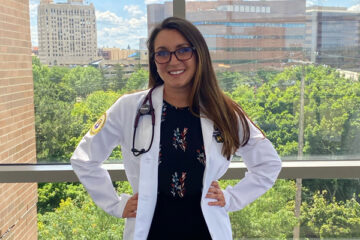 Brittany Douglas poses in w white lab coat in the William S. White Building on UM-Flint's campus