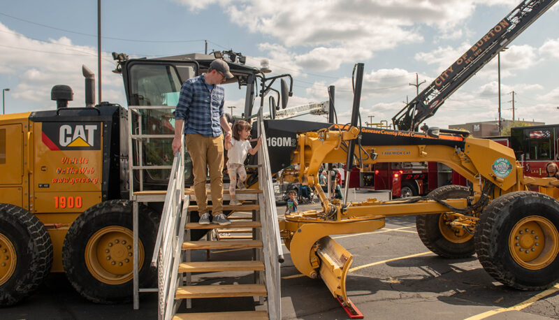 A father and daughter climbing the steps to a back hoe