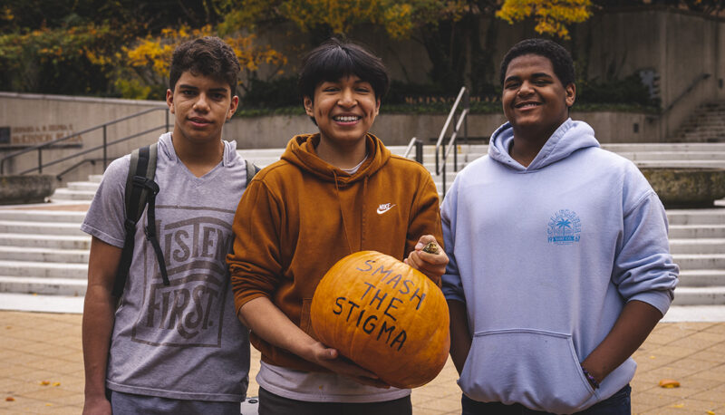 Three students posing with a pumpkin with the words "Smash the stigma" written on it.