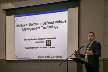 A man in a suit stands at a podium to the right of a large screen that says, "Intelligent Software Defined Vehicle Management Technology"