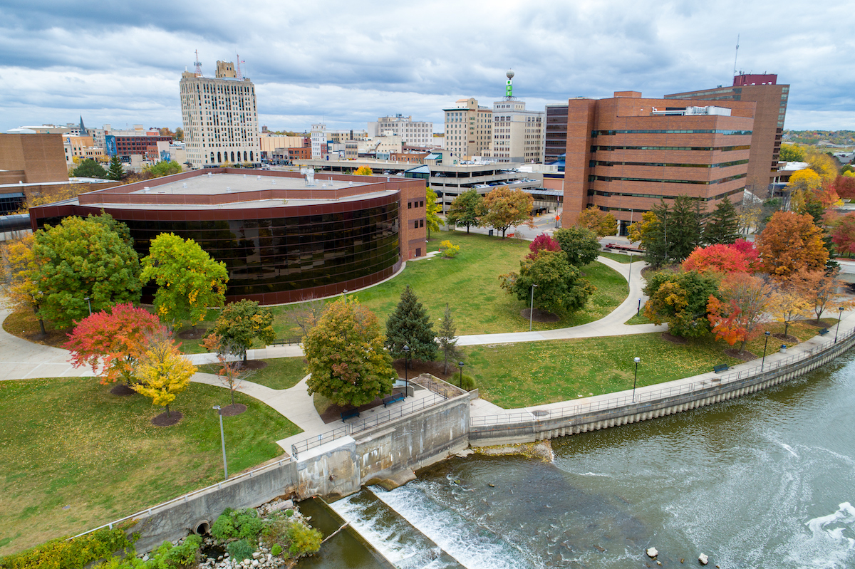 An aerial view of the University of Michigan-Flint campus in autumn, showing the Flint River and Thompson Library.