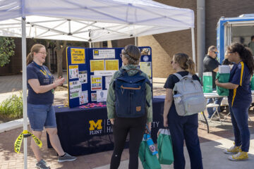 Students talking with a presenter at a table outside