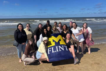 Students and faculty posing with a UM-Flint flag on a beach