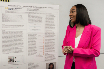 Jamiah McQuiller in a pink blazer speaking in front of her research poster.