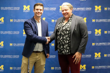 Two people shaking hands in front a UM-Flint banner