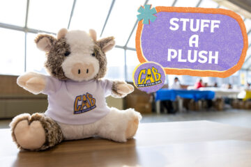 A plushie cow on a table with a Stuff Plush graphic