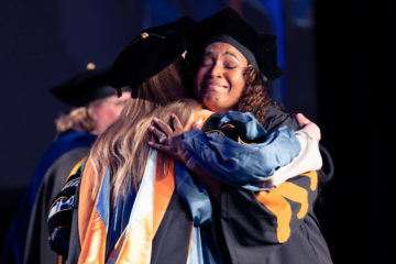 A graduating student hugging a professor in regalia.