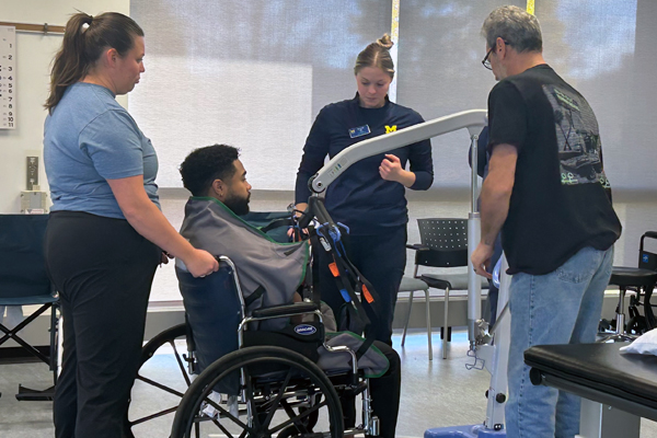 Three physical therapy students demonstrate using a hoyer lift during a lab for ALS caregivers.