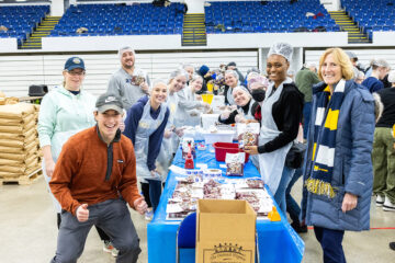 UM-Flint faculty and students posing for a photo while assembling meals.