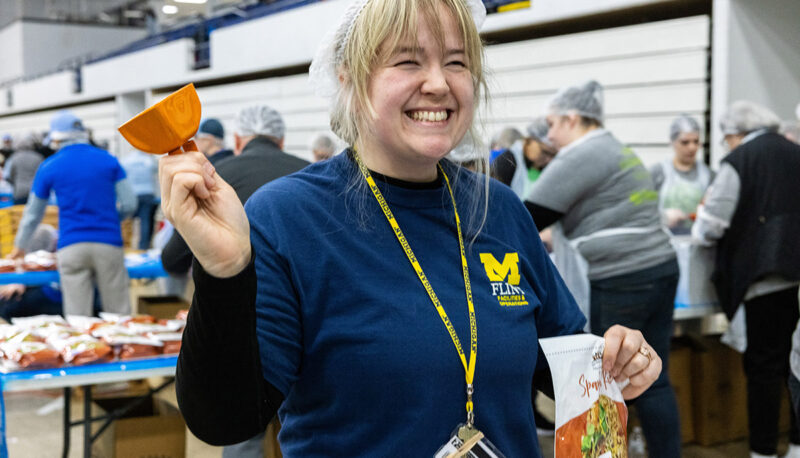 A UM-Flint student posing while assembling meals