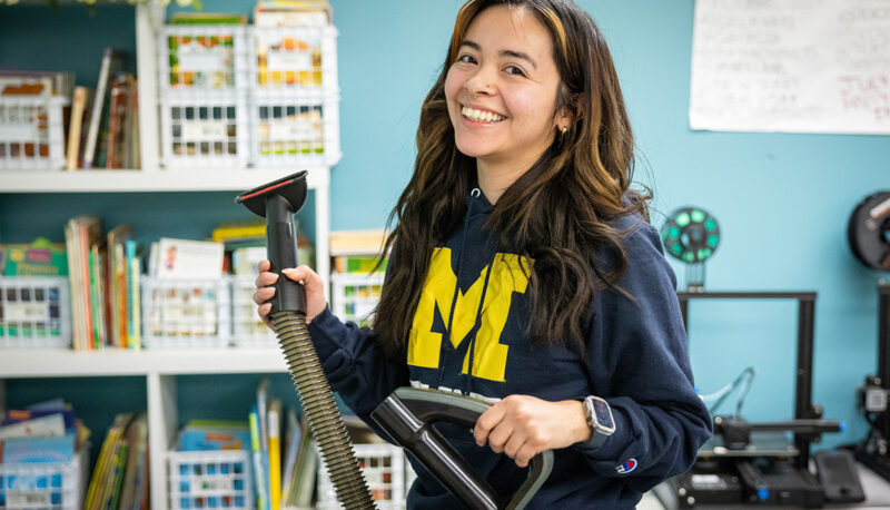 A UM-Flint student smiling with a vacuum cleaner