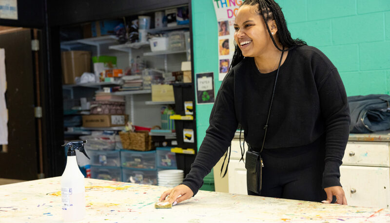 A UM-Flint student smiling while wiping down a table.