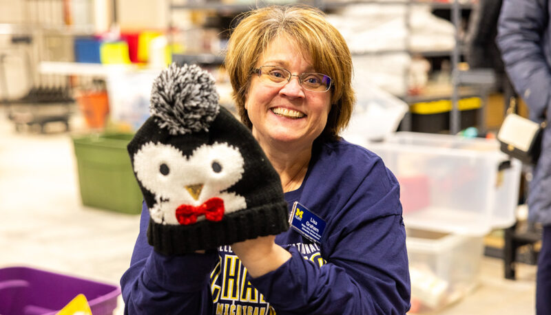 A UM-Flint faculty or staff member posing with a penguin beanie hat.