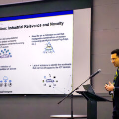 Kessentini stands to the right of the image facing a podium. Behind him, there is a large screen that says, "Problem: Industrial Relevance and Novelty" and says what some of the issues with computing in automobiles are currently, with images. Of a car, of a pyramid chart, of IoT device icons, and another showing how those devices are all part of the car's processing workload.