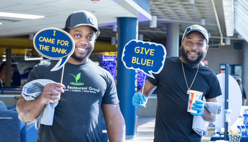 Two staff members holding up sings that say "I came for the bank" and "Give Blue"