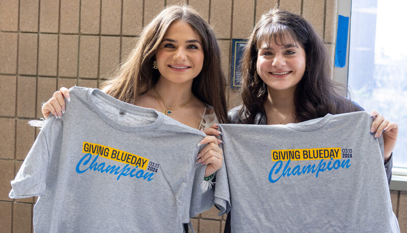 Two female students holding up Giving Blueday Champion t shirts