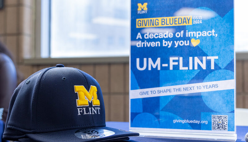 A UM-Flint hat on a table next to a Giving Blueday sign