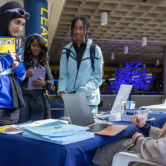 A group of female students talking to another student sitting at a Giving Blueday table