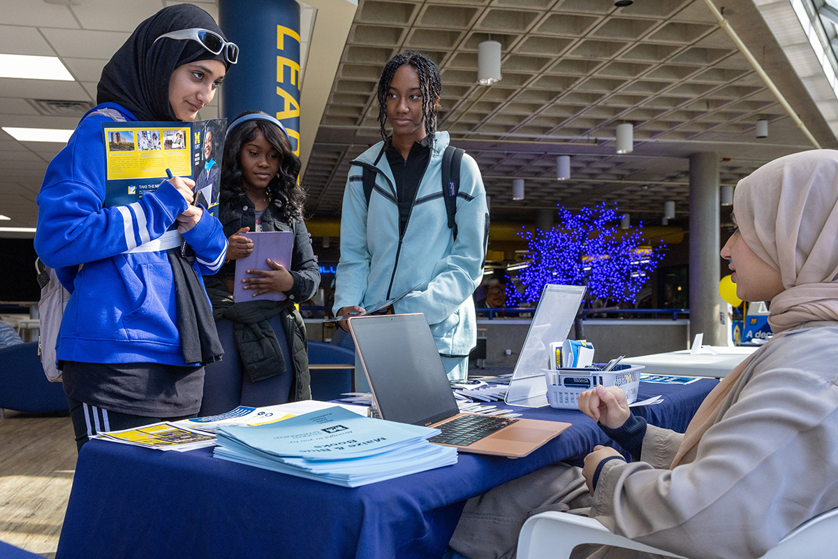 A group of female students talking to another student sitting at a Giving Blueday table