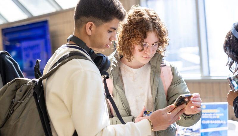 Two students looking at a phone in front of the Giving Blueday Tabes