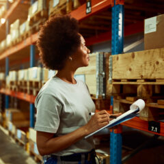 A woman with a clipboard looking at pallets in a warehouse.