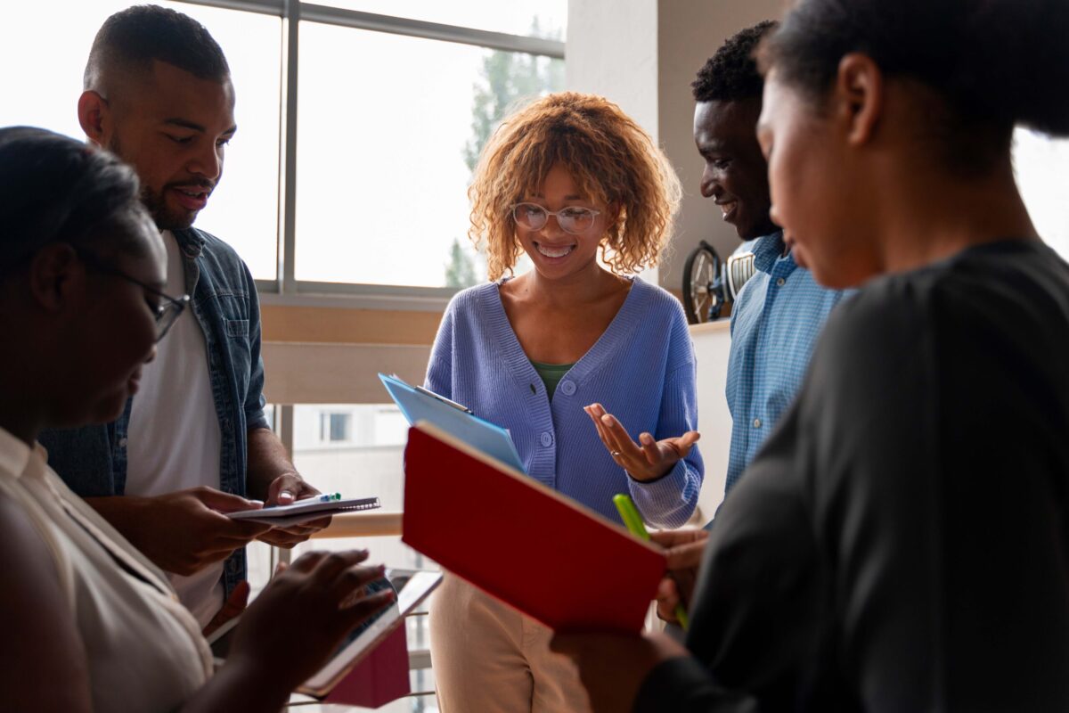 A group of people standing in a circle talking while referencing paperwork.