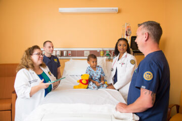 Four nursing students smiling around a hospital bed with a young child in it.