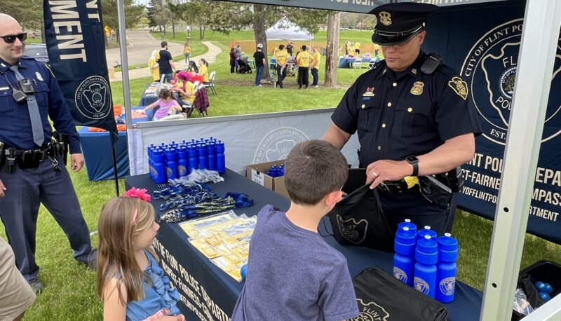 Young Officer Friendly Day attendees talking with a police officer behind a table.