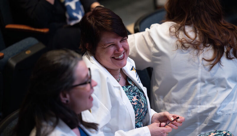 Students in their white lab coats laughing during the ceremony.