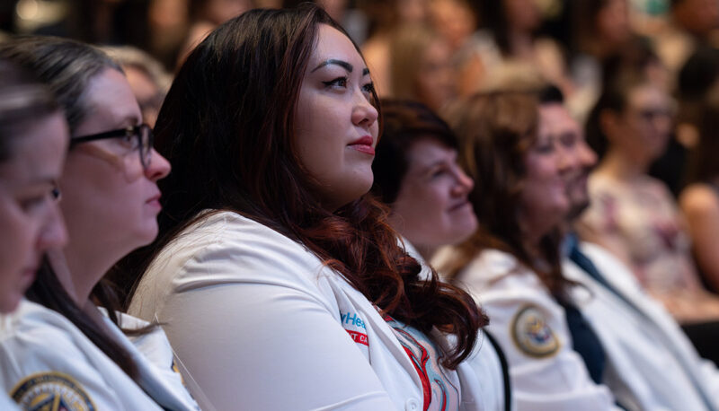 Students in white lab coats looking on in the audience.