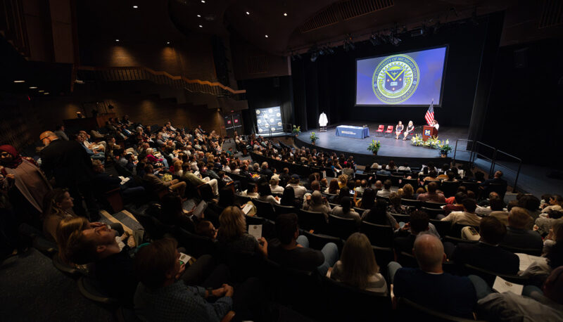 A wide shot of the seated crowd and stage during the white coat ceremony.