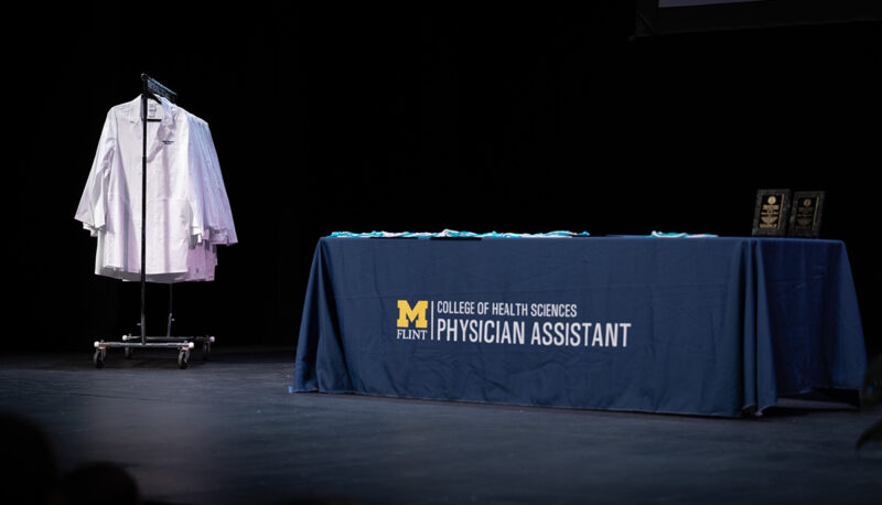 An empty stage showing a table with a PA program tablecloth and rack of white coats.