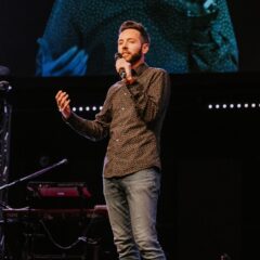 Joshua Spencer speaking into a microphne on stage.