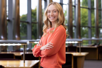 A young woman smiling with her arms folded, looking at the camera