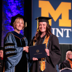 A female student receiving her diploma onstage from interim chancellor Dnna Fry