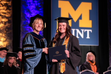 A female student receiving her diploma onstage from interim chancellor Dnna Fry