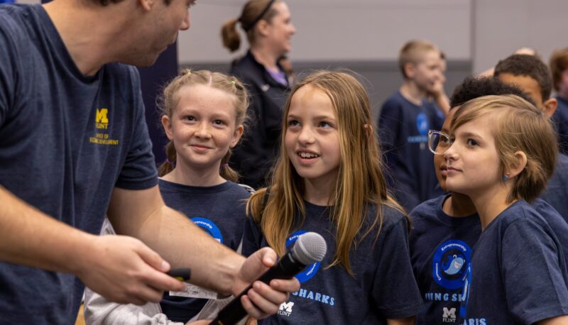 UM-Flint staff member Nic Custer with a microphone talking with Young Sharks participants.