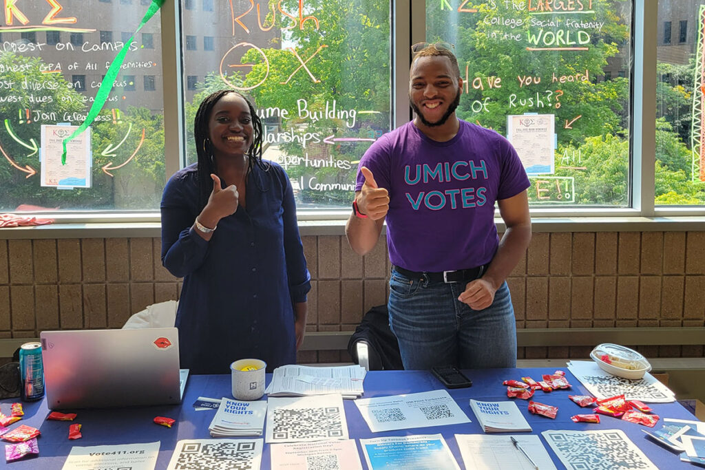 Alimatou Sarr and Myron Henderson standing behind a table encouraging people to vote. 