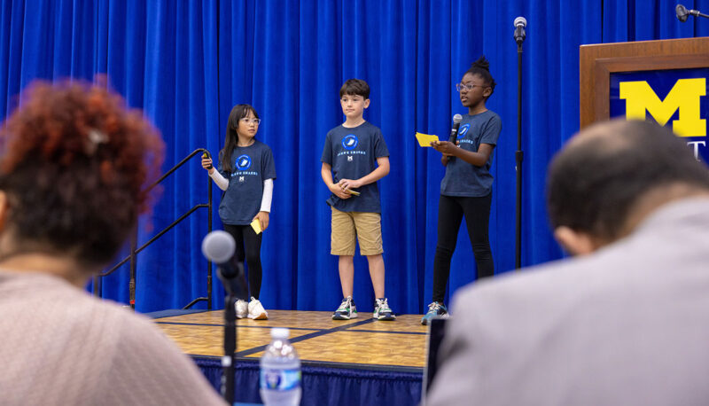 A team of young students presenting their project on stage while judges look on.